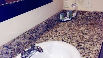 A bathroom with a white sink, granite countertop, and a hairdryer mounted on the wall.