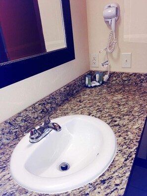 A bathroom with a white sink, granite countertop, and a hairdryer mounted on the wall.