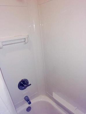 A small, white, enclosed shower area with a built-in shelf and a faucet.