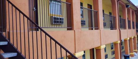 A multi-story building with a yellow facade, multiple balconies, and a staircase leading to the upper floors.