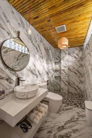 Un bagno con un mobile lavabo in marmo, uno specchio rotondo, un WC e una zona doccia.