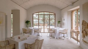 A spacious dining area with high ceilings and large windows, featuring white tables and wicker chairs. - Es Racó D Artá (Arta)