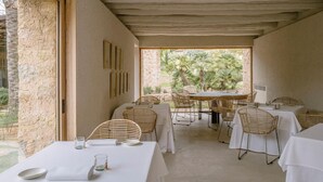 An outdoor dining area with tables and wicker chairs, surrounded by stone walls and a view of greenery. - Es Racó D Artá (Arta)