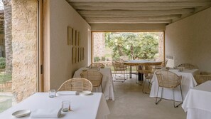 An outdoor dining area with tables and wicker chairs, surrounded by stone walls and a view of greenery. - Es Racó D Artá (Arta)