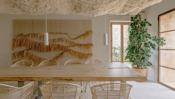A dining area with a large wooden table, wicker chairs, a hanging light fixture, and a large wall art piece. - Es Racó D Artá (Arta)