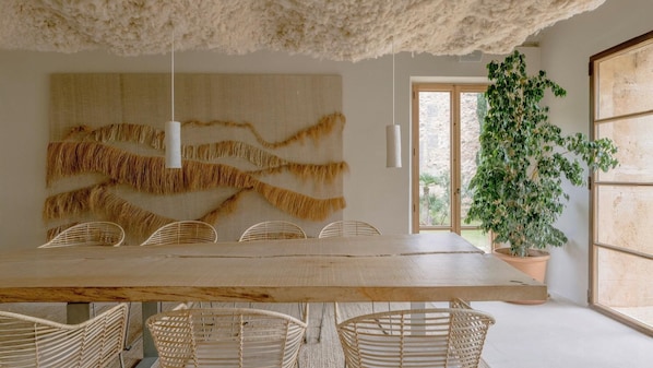 Ein Essbereich mit einem großen Holztisch, Korbstühlen, einer Hängelampe und einem großen Wandbild.