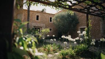 A courtyard with a stone building, a pergola, and flowering plants.