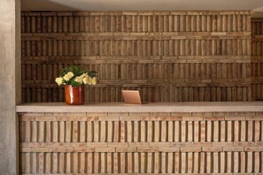 A reception desk with a brick wall backdrop, a potted plant, and a laptop. - Hotel Humano (Santa María Colotepec)