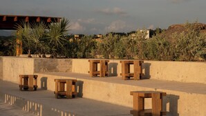 Outdoor wooden benches aligned against a concrete wall with a backdrop of vegetation and buildings. - Hotel Humano (Santa María Colotepec)