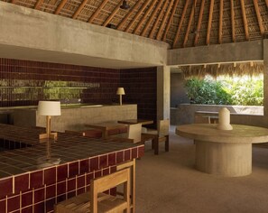 A modern interior with a thatched roof, a tiled bar area, and a view of greenery outside. - Hotel Humano (Santa María Colotepec)
