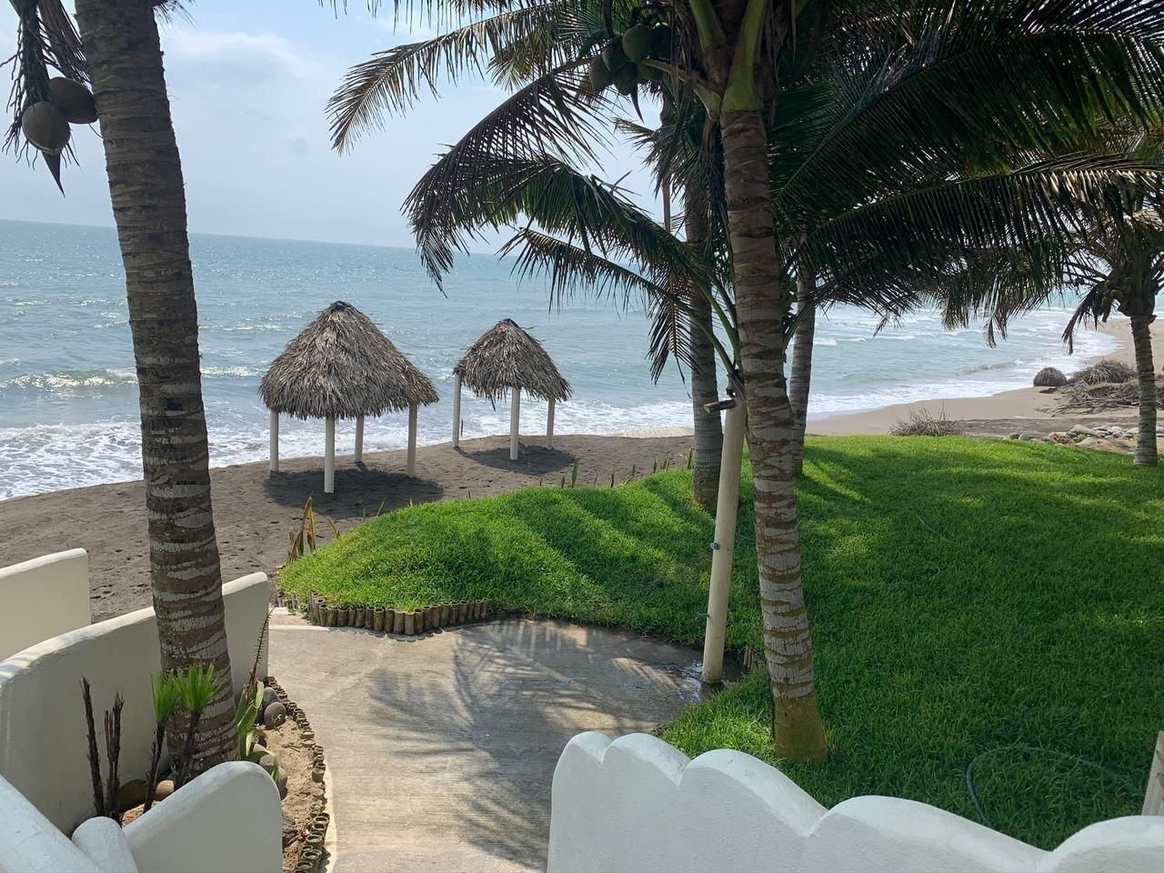 Vista de una playa con palmeras, chozas de paja y un camino de concreto que lleva a la orilla.