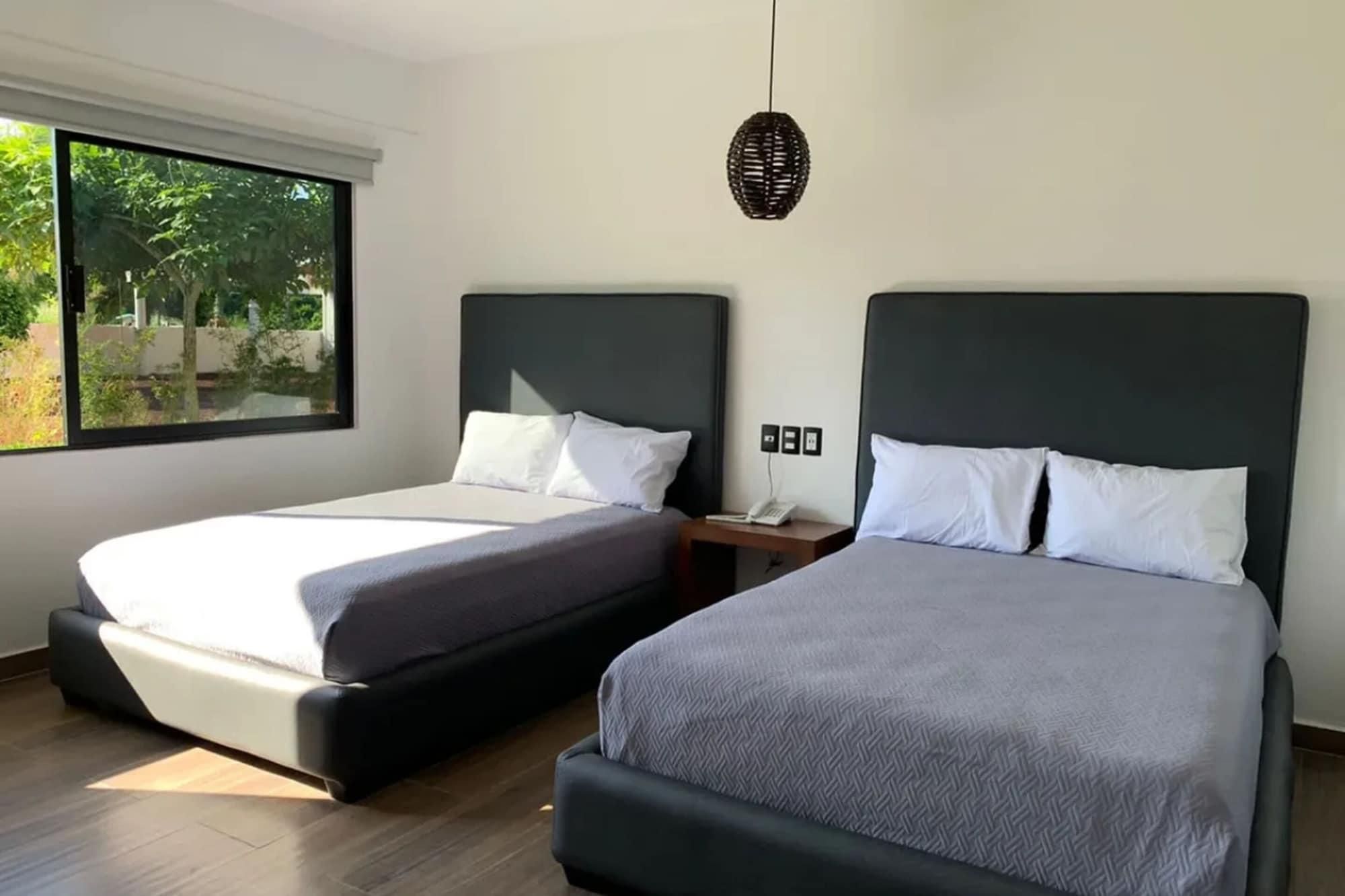 A hotel room with two beds, a large window, and a hanging light fixture.