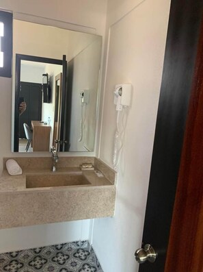 Un bagno con lavandino, specchio, asciugamano e zona doccia visibile attraverso una porta aperta.