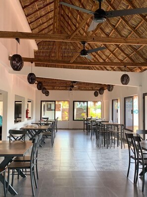 Un'ampia sala da pranzo con soffitti alti, travi a vista in legno e grandi finestre che offrono vista sul paesaggio.