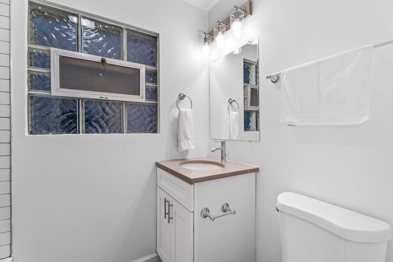 A bathroom with a sink, mirror, towel rack, and a window with frosted glass.