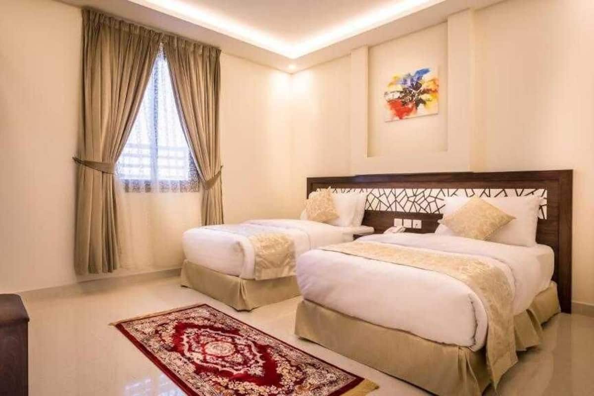 Ein Hotelzimmer mit zwei Betten, einem hölzernen Kopfteil, einem Teppich mit rotem und weißem Muster und einem Fenster mit Vorhängen.