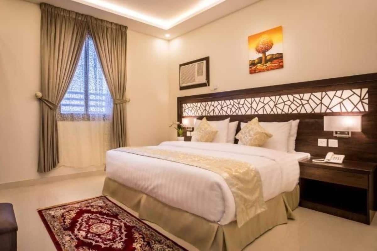 Ein Hotelzimmer mit einem großen Bett, einem Nachttisch mit Telefon, einem Schreibtisch mit Stuhl, einem Fenster mit Vorhängen und einem Bild an der Wand.