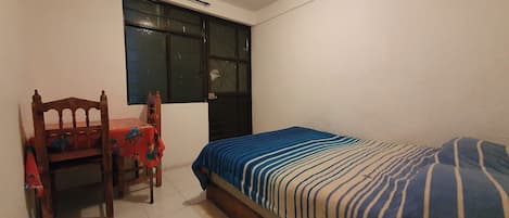 Un dormitorio con cama, una silla, una mesa y un ventanal.