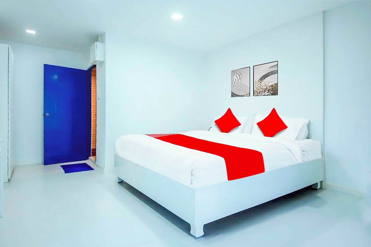 A modern hotel room with a white bed, red pillows, and a blue door.