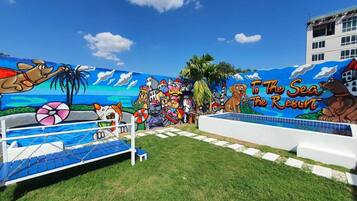 Une fresque murale sur le thème de la plage, avec une piscine, des palmiers et un panneau indiquant « To The Sea Resort ».
