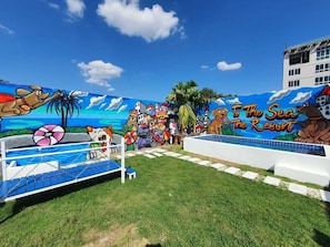 A beach-themed mural with a pool area, palm trees, and a sign reading "To The Sea Resort". - Collection O To The Sea Resort Thailand (Sattahip)