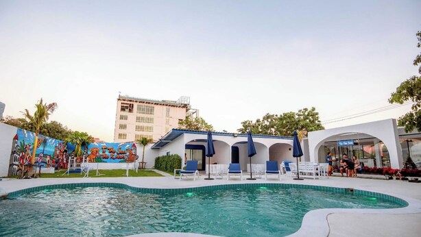 A swimming pool with lounge chairs and umbrellas, a mural, and a building with a sign. - Collection O To The Sea Resort Thailand (Sattahip)