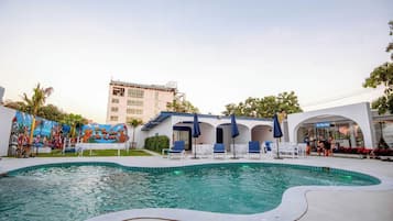 A swimming pool with lounge chairs and umbrellas, a mural, and a building with a sign.