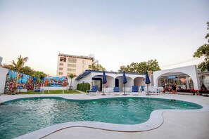 Una piscina con sillas de descanso y sombrillas, un mural y un edificio con un letrero.