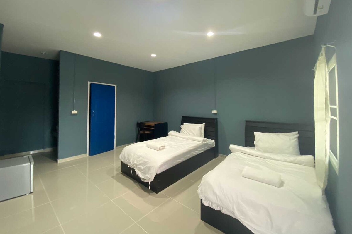 A modern hotel room with two beds, a desk, and a blue door.