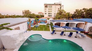 A swimming pool with lounge chairs and umbrellas, surrounded by a landscaped garden and a building with a mural. - Collection O To The Sea Resort Thailand (Sattahip)