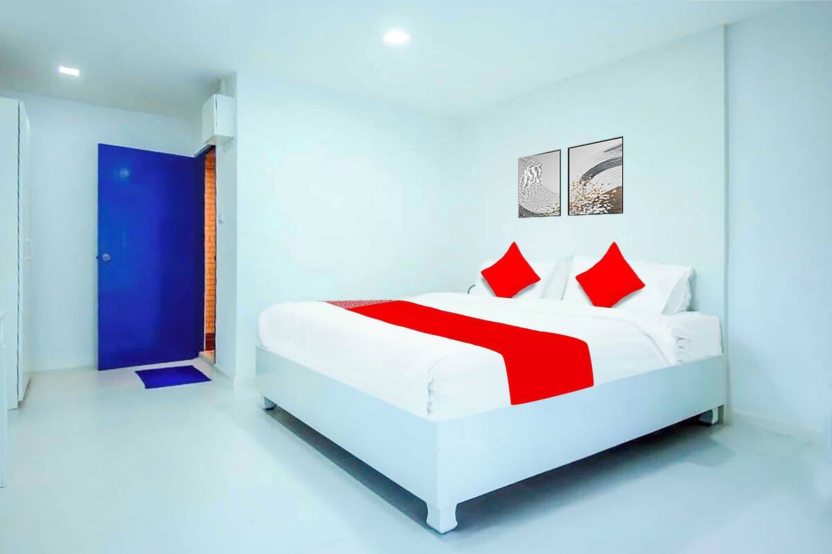 Ett modernt hotellrum med en vit säng, röda kuddar och en blå dörr.
