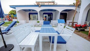 An outdoor seating area with white and blue furniture, a covered patio, and a building with a blue roof and white walls. - Collection O To The Sea Resort Thailand (Sattahip)