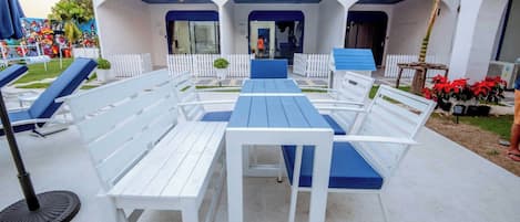 An outdoor seating area with white and blue furniture, a covered patio, and a building with a blue roof and white walls.