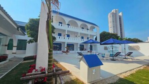 A hotel courtyard with a pool, lounge chairs, and a palm tree. - Collection O To The Sea Resort Thailand (Sattahip)