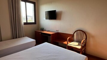 Habitación de hotel con cama, escritorio, silla, televisor montado en la pared y ventana con cortinas.