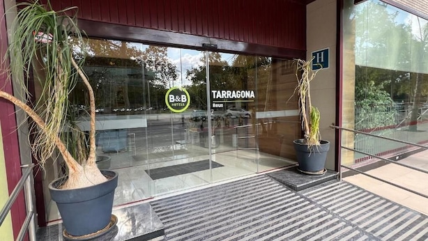 The entrance to B&B Hotels with a clear glass door, two potted plants, and a visible parking area. - B&b Hotel Tarragona Reus  (Reus)