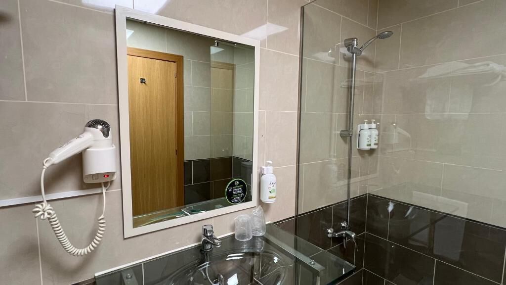 A modern bathroom with a glass shower enclosure, a hairdryer mounted on the wall, and a mirror above the sink.