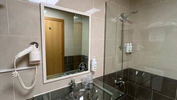 A modern bathroom with a glass shower enclosure, a hairdryer mounted on the wall, and a mirror above the sink.