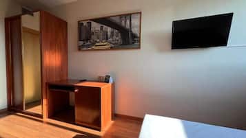 Een kamer met een houten bureau, een spiegel, een stadsbeeld in een lijst en een televisie aan de muur.