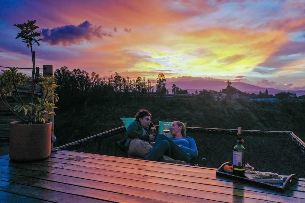 Zwei Personen sitzen auf einer Holzdiele mit Blick auf einen Sonnenuntergang.