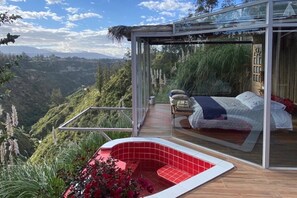 A modern bedroom with a glass enclosure, a red hot tub, and a bed with a view of a mountainous landscape. - Samay Collections (Tababela)