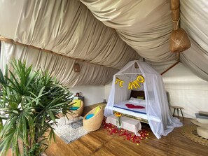 A cozy room with a canopy bed, a large potted plant, and a small table with a vase of flowers. - Samay Collections (Tababela)