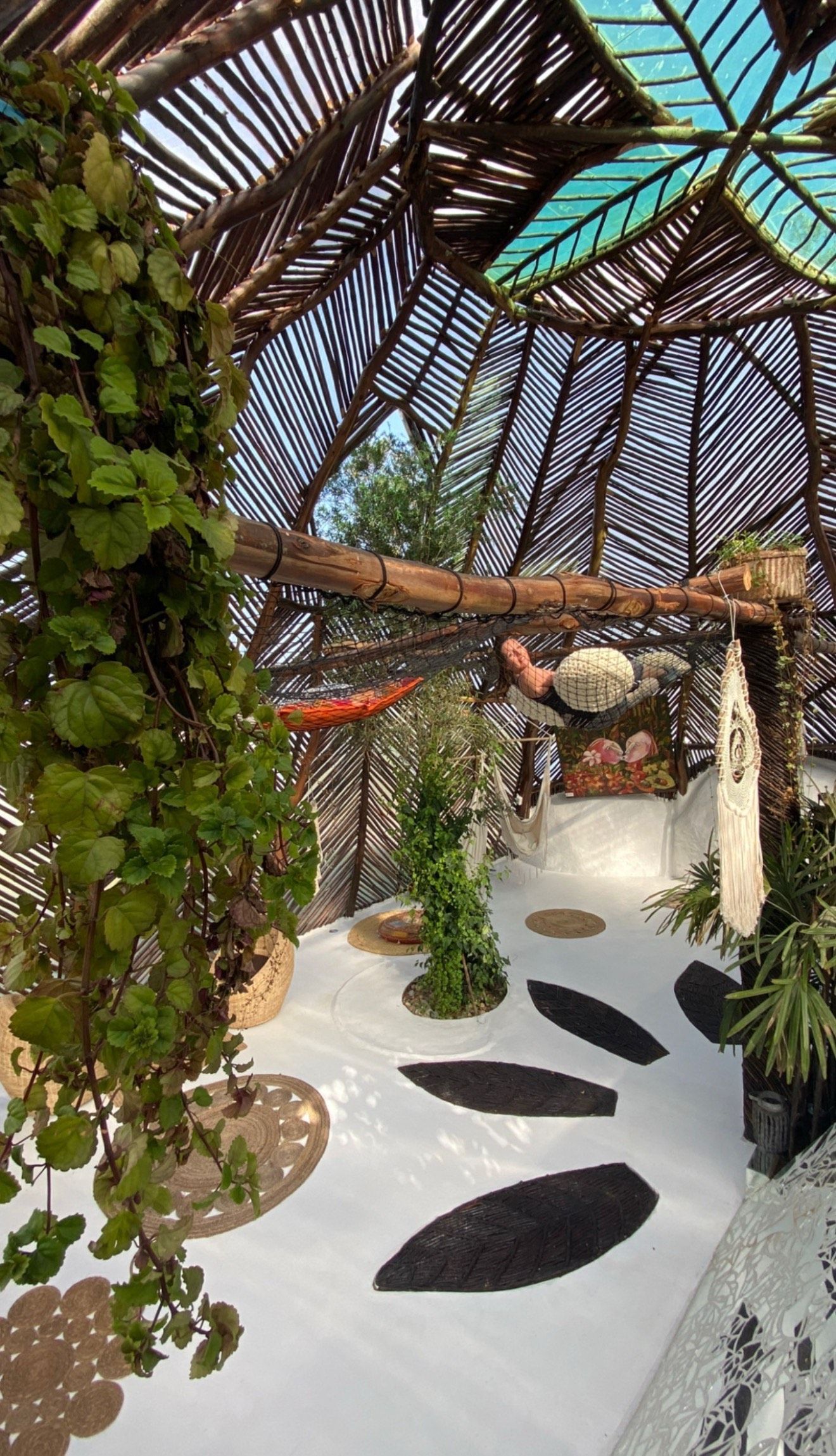 A covered outdoor area with a thatched roof, bamboo structures, and various potted plants.