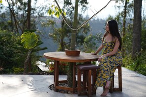 A woman sitting at a wooden table with a potted plant, surrounded by greenery. - Samay Collections (Tababela)