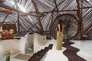 A modern interior with a geometric ceiling structure, a staircase with a unique design, and a large mirror reflecting the space. - Samay Collections (Tababela)
