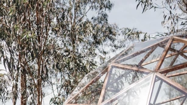 A geodesic dome structure with a wooden floor and a bed inside. - Samay Collections (Tababela)