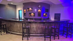A bar area with a curved counter, multiple framed pictures on the wall, and bar stools. - Golden Beach Hotel (M'diq)