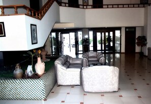 A spacious lobby with a modern staircase, leather sofas, and a patterned bench. - Golden Beach Hotel (M'diq)