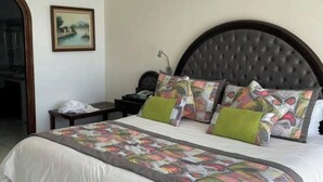 Un letto rifatto con una coperta a motivi e numerosi cuscini, una testiera scura, un comodino con una lampada e un quadro incorniciato appeso al muro.