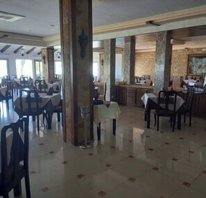 A spacious dining area with multiple tables and chairs, large pillars, and a tiled floor.